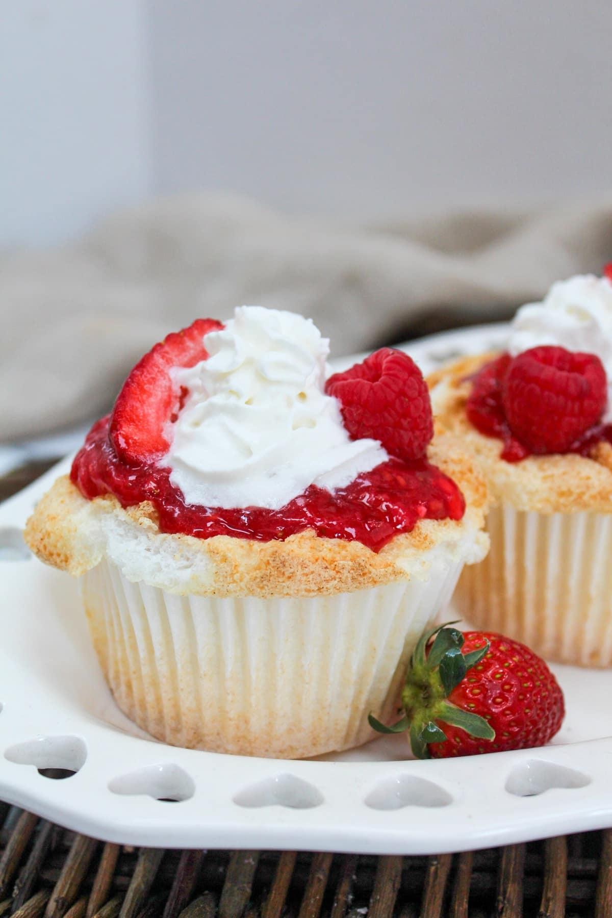 cupcake on a white plate with a strawberry on the side.