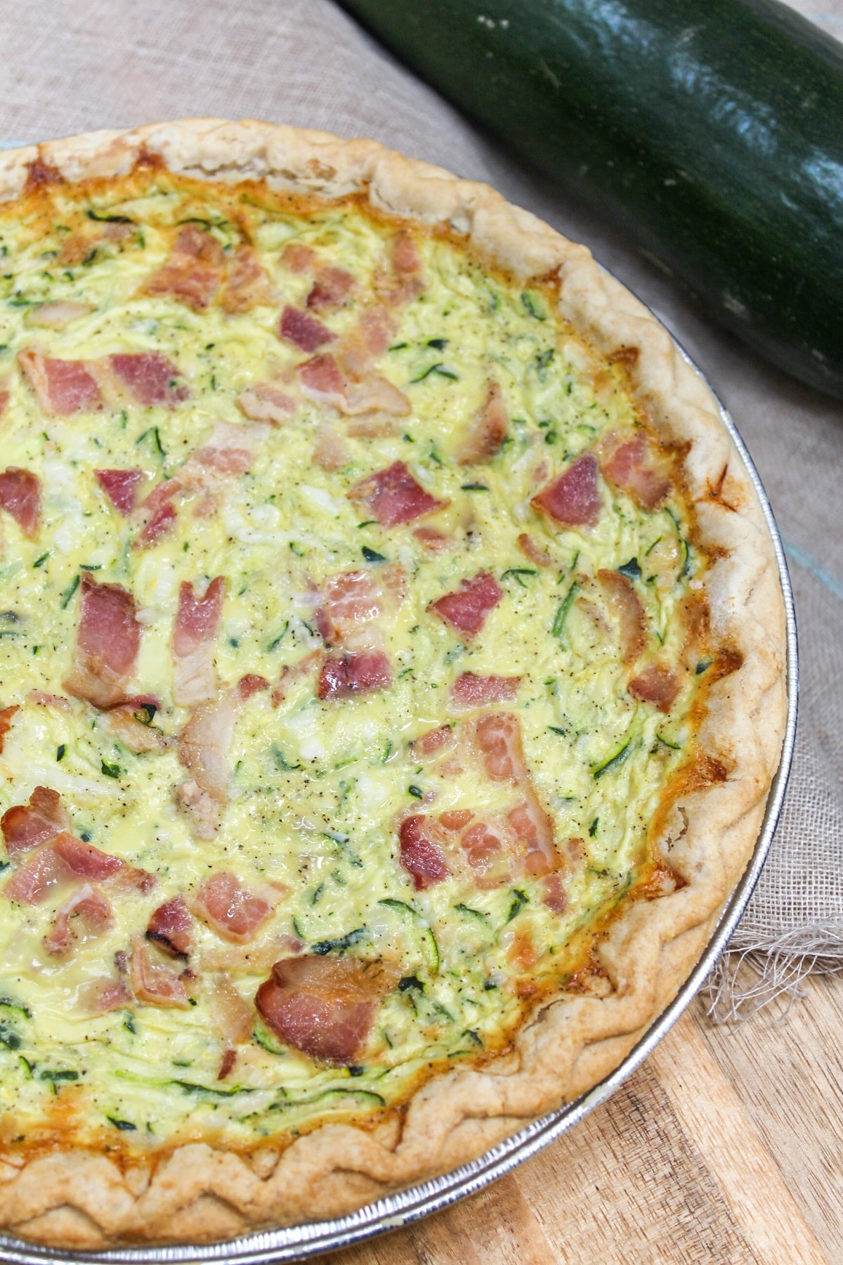 quiche filled with shredded zucchini and bacon. Placed on a cutting board with fresh zucchini on the side. 