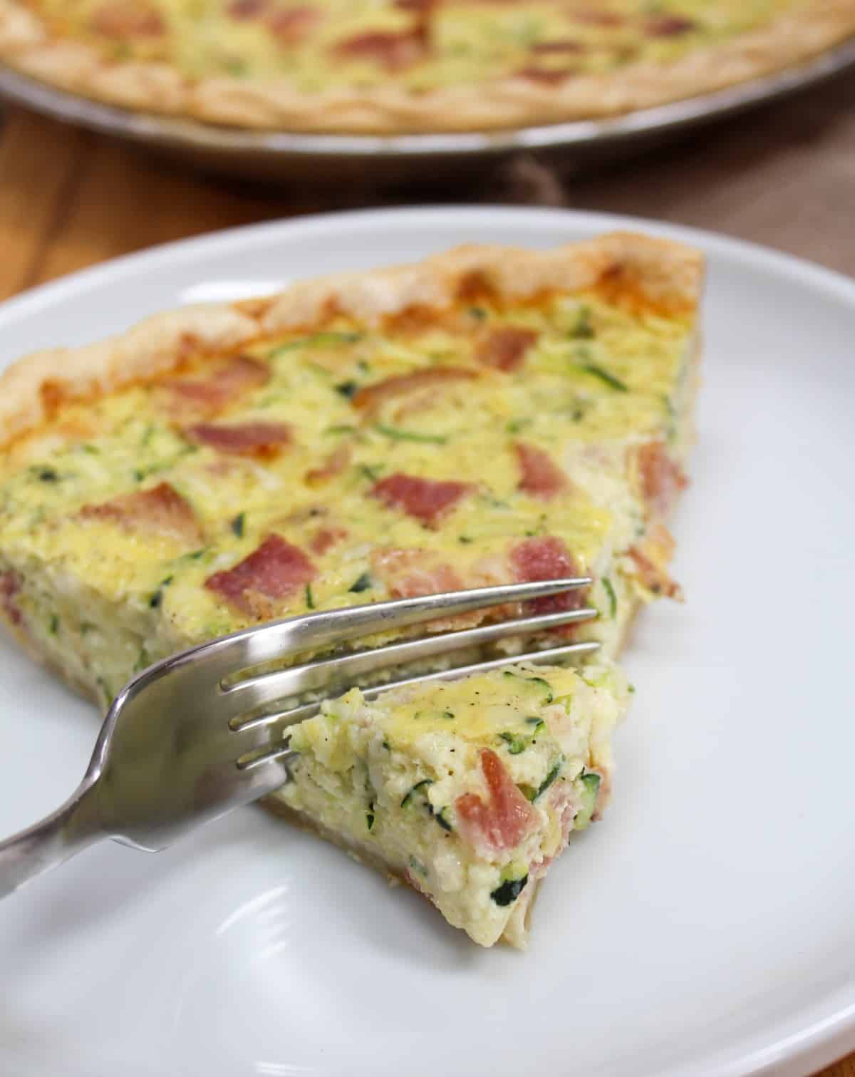 Sliced quiche on a white plate with a fork cutting a bite.