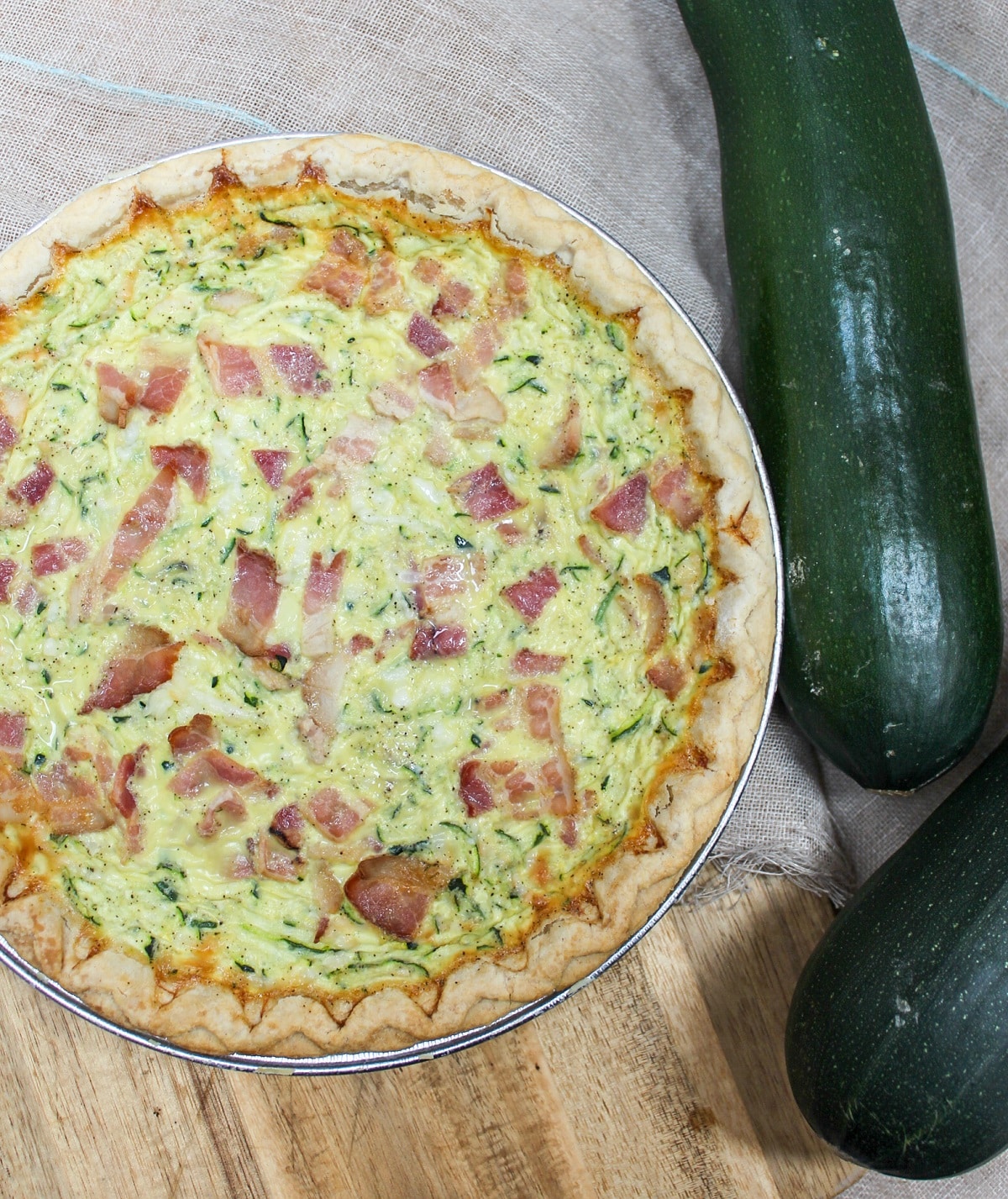 quiche filled with shredded zucchini and bacon. Placed on a cutting board with fresh zucchini on the side.