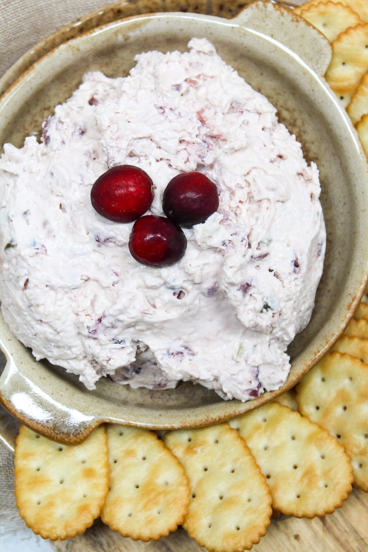 pink cranberry jalapeno dip topped with fresh cranberries on a bowl. Crackers are served on the side of the bowl.