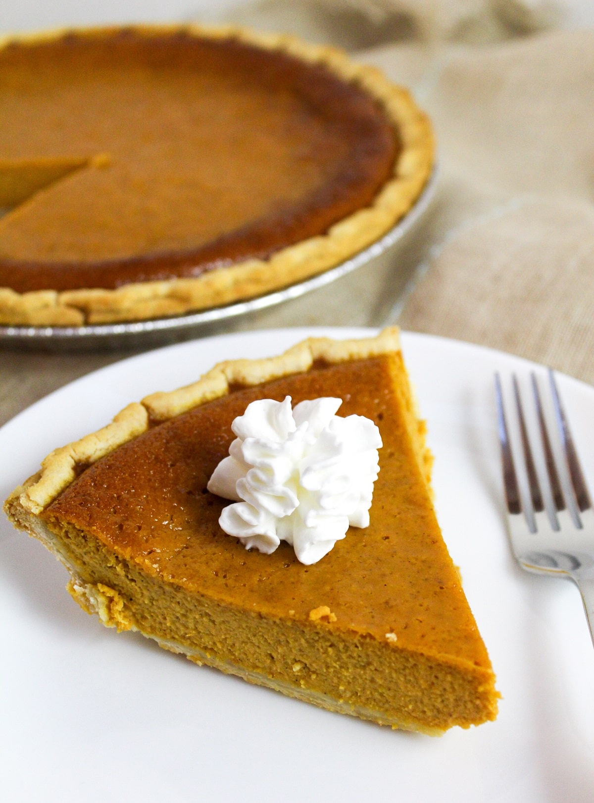 pumpkin pie on a white plate with whipped cream.