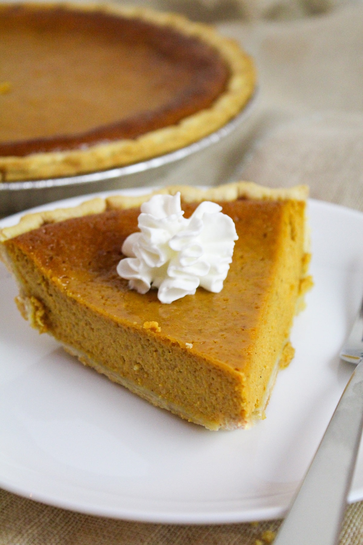 pumpkin pie on a white plate with whipped cream.