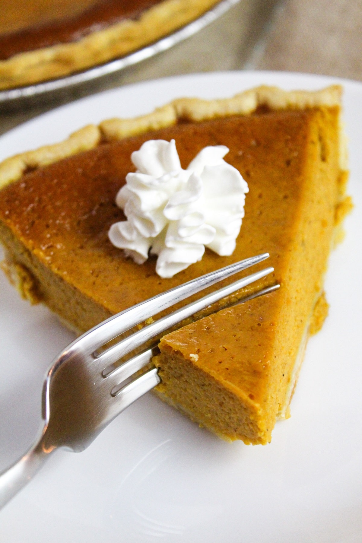 pumpkin pie on a white plate with whipped cream cut with a fork.