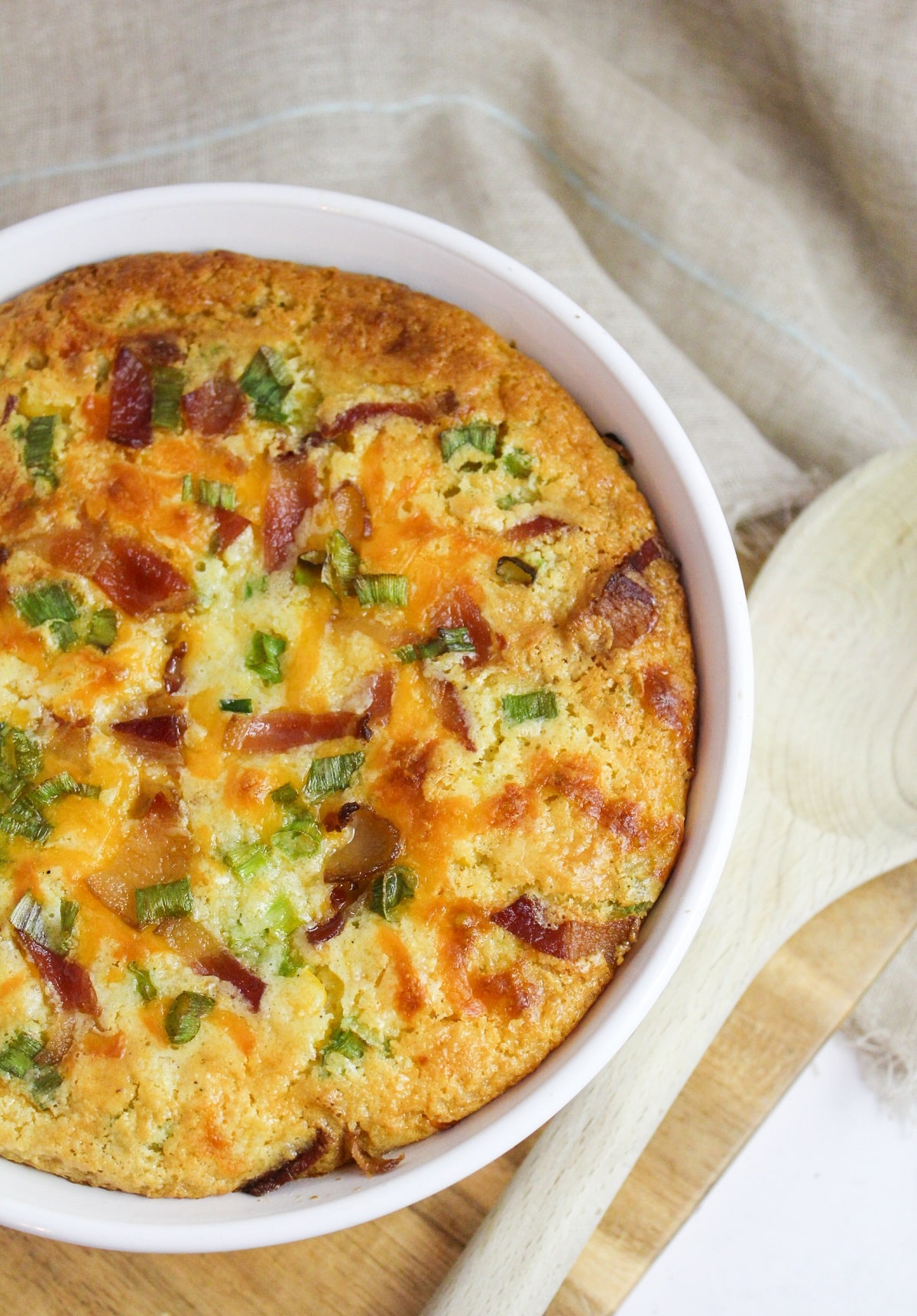 corn casserole topped with bacon, green onion, and cheese in a white baking dish.