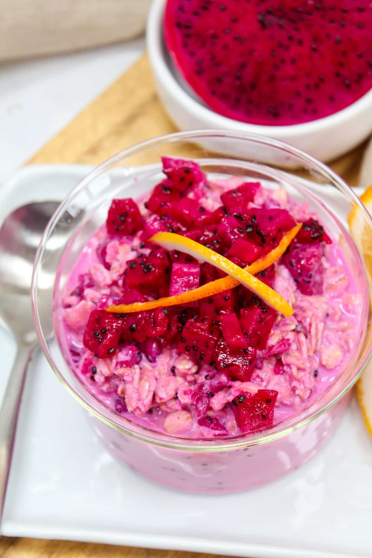 Pink overnight oats topped with chopped dragon fruit and citrus zest in a glass bowl. 
